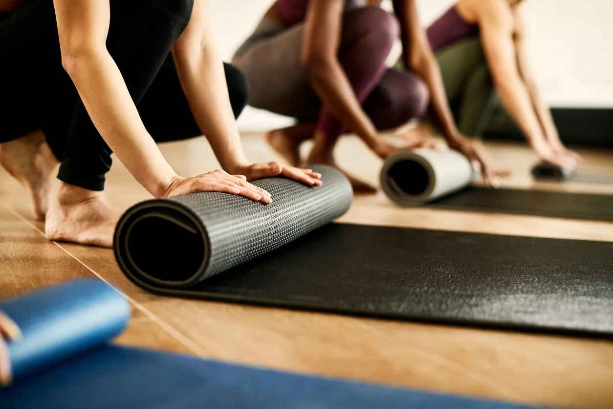 Students rolling out their mats before a yoga class on warm wood floors